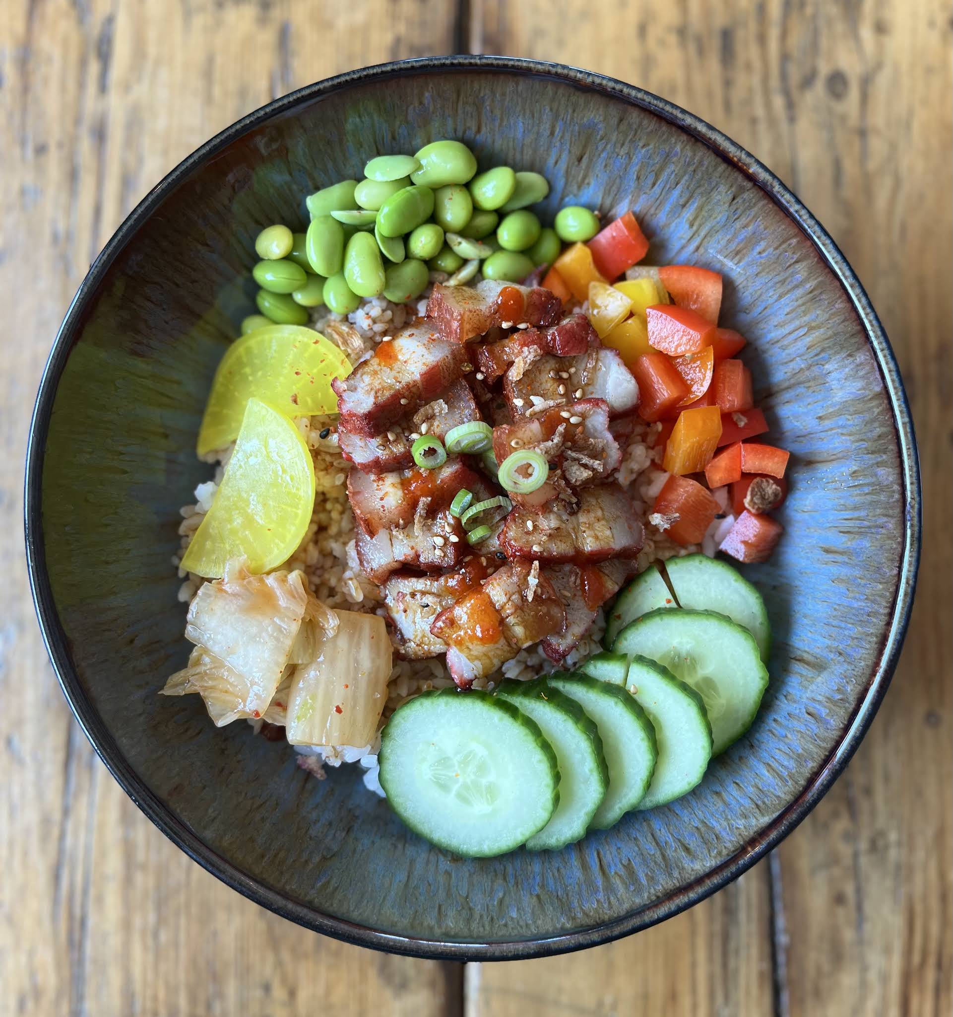 A complete ceramic bowl of rice with sliced meat, cucumber, edamame and colourful vegetables photographed by Graze Cafe